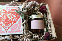 The Perfect Match Gift Box by Wild About Flowers includes a floral card with a red heart, Coconut & Geranium soy candle, dried flowers, and brown crinkle paper—an ideal and thoughtful Valentine's Day gift.
