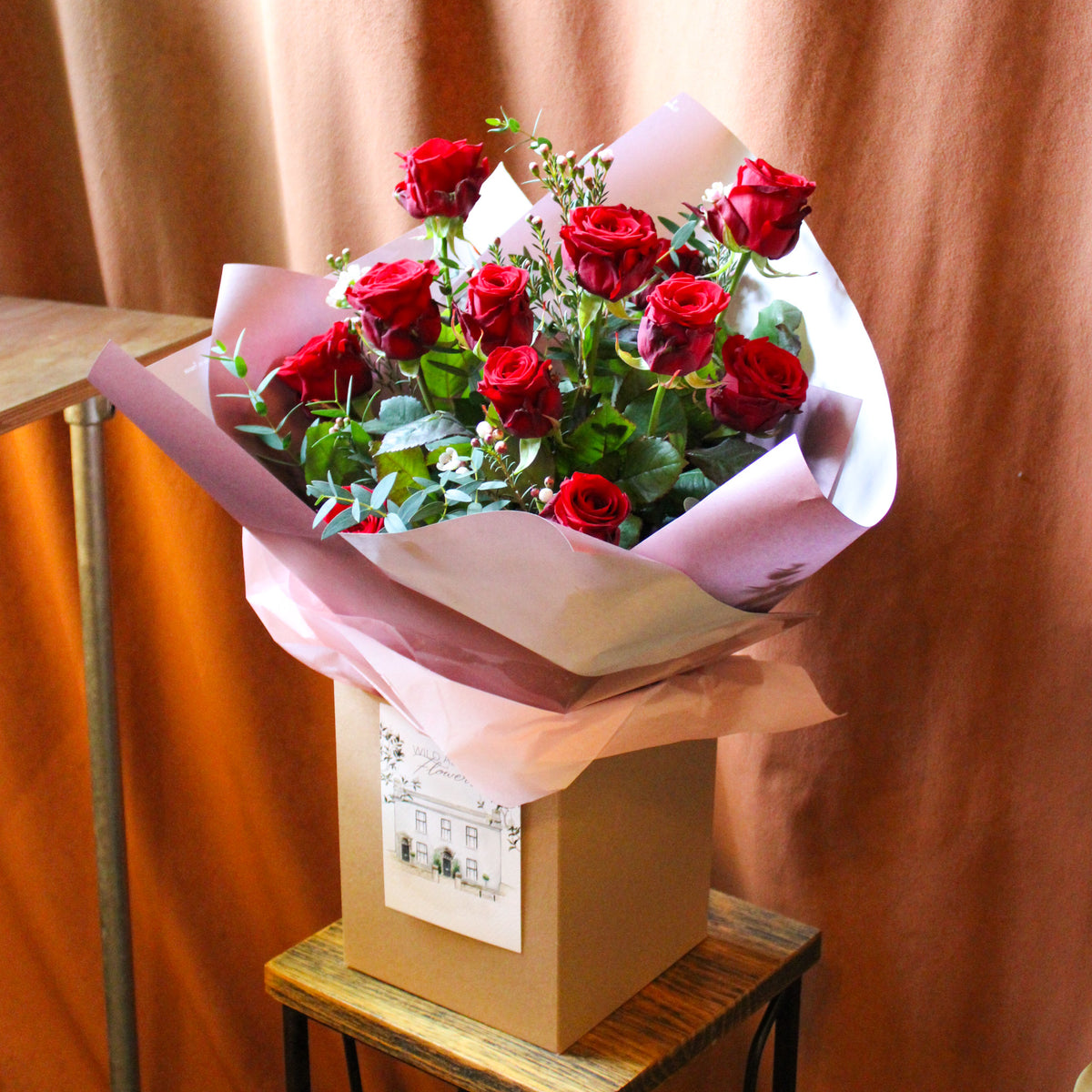 The Ultimate Valentine Red Rose Bouquet by Wild About Flowers features luxury red roses with greenery, wrapped in pink and purple paper, beautifully gift-boxed—perfect Valentine’s Day flowers.