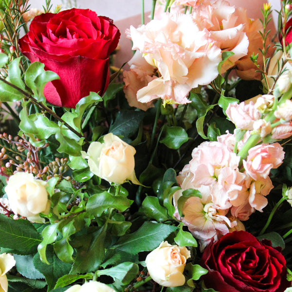 The 'Vintage Muse' Fresh Flower hand tied bouquet by Wild About Flowers features red roses, pale pink carnations, and cream spray roses with lush greenery, capturing timeless elegance.