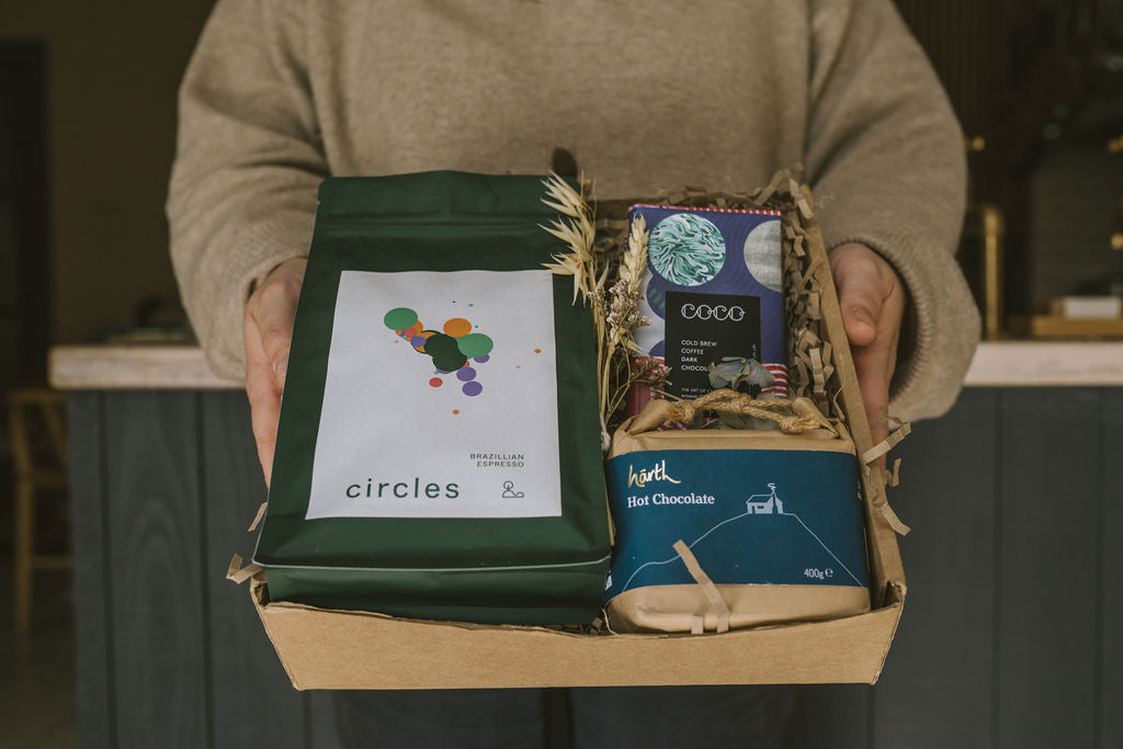 Person holding a gift box containing coffee, dark chocolate and hot chocolate