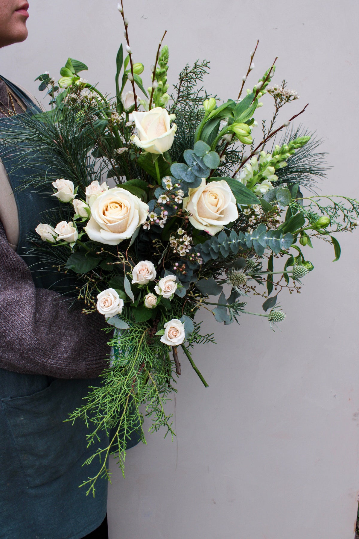 A person in gray holds the Wilder One Christmas Bouquet by Wild About Flowers, featuring white roses, winter blooms, greenery, and eucalyptus—perfect for the season from your local Keynsham florist.