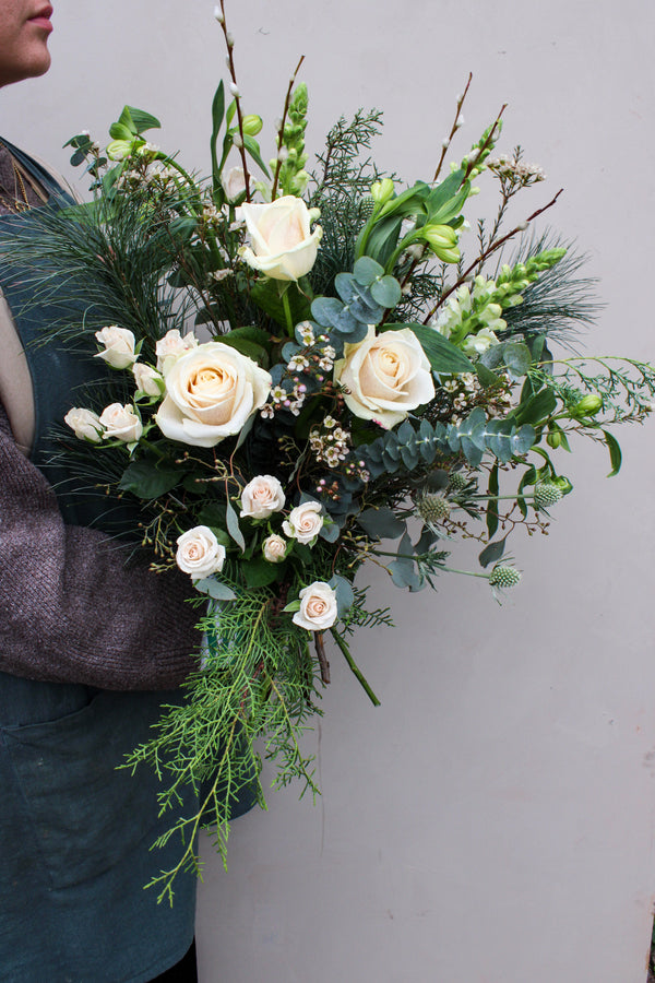 A person in gray holds the Wilder One Christmas Bouquet by Wild About Flowers, featuring white roses, winter blooms, greenery, and eucalyptus—perfect for the season from your local Keynsham florist.
